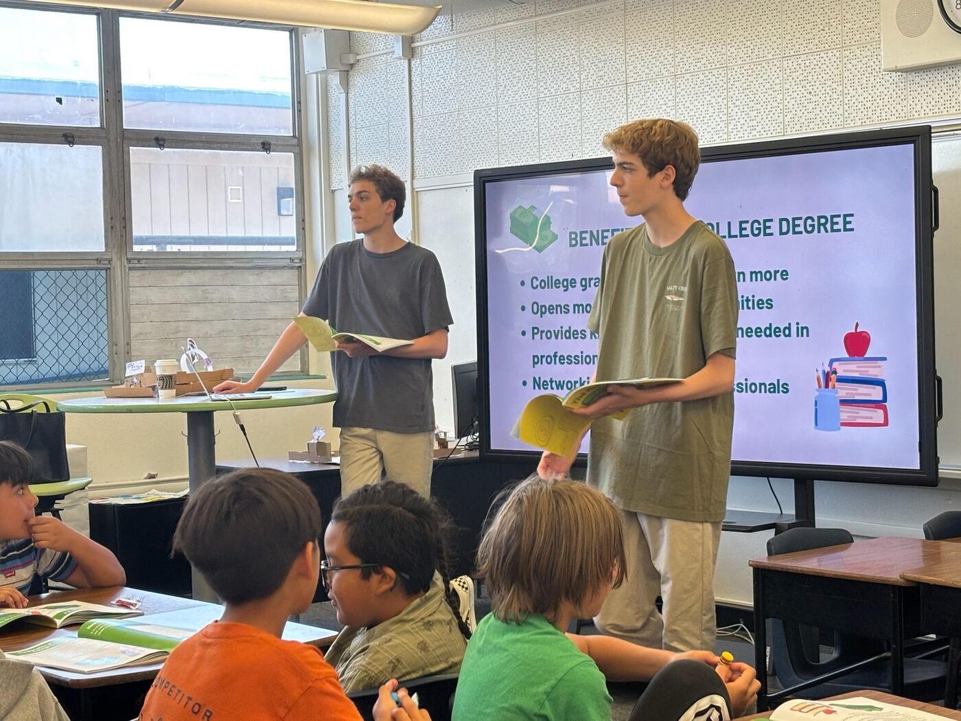 Luke and Nick teaching at the front of a classroom beside a slide on the benefits of a college degree